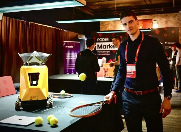 Sportbot founder standing beside the Sportbot machine at a conference stand